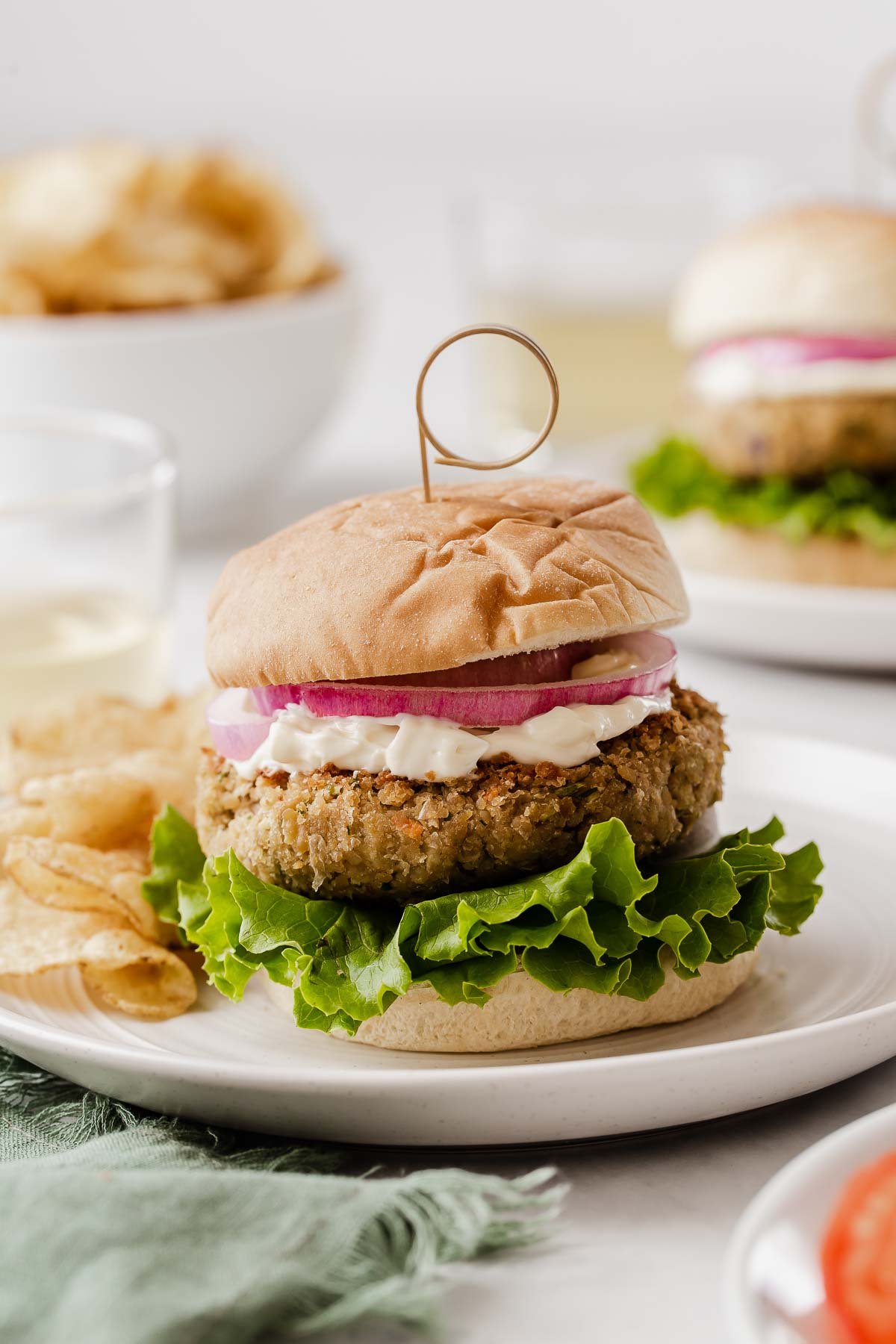 Vertical image of chickpea burgers on bun with lettuce, mayo and a slice of tomato.
