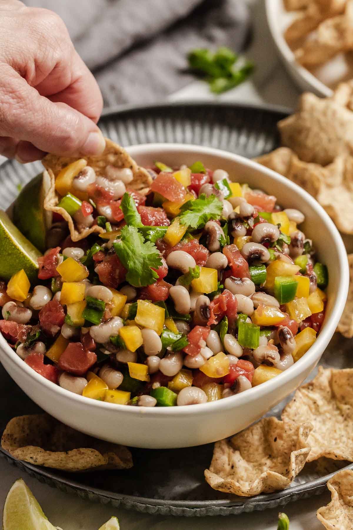 Hand scooping up Texas Caviar onto a bowl shaped chip.