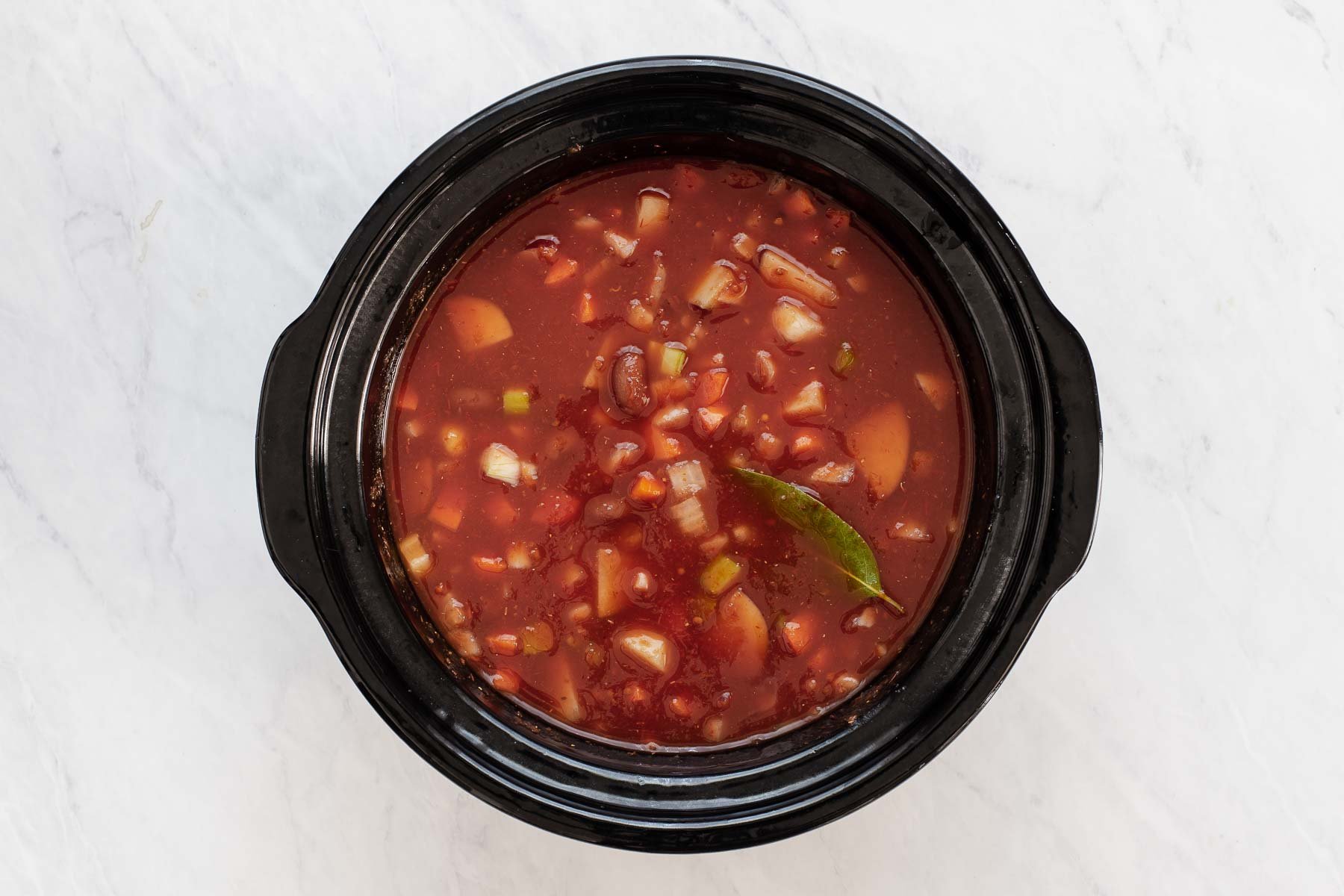 Tomato broth vegetable bean soup in black round slow cooker.