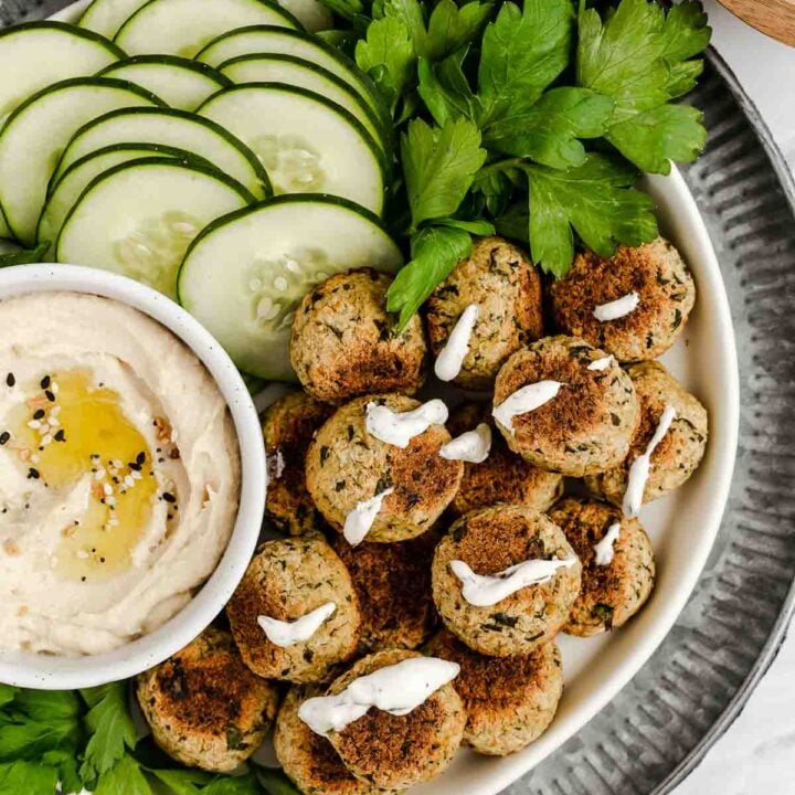 Vertical shot of baked falafel with sliced cucumber and hummus dip.