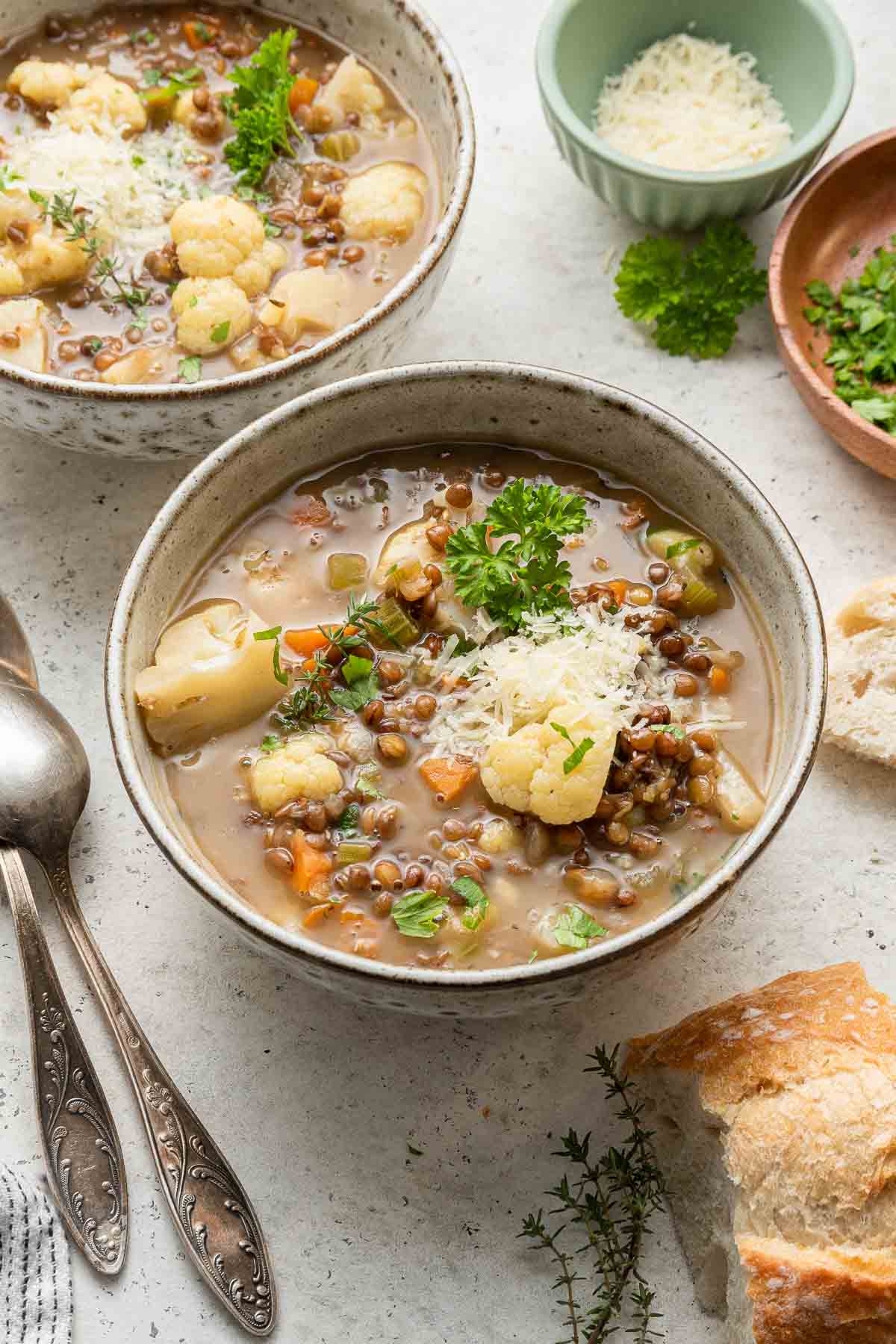 Side angle shot of a bowl of hearty soup on stone background with bread and spoons alongside.