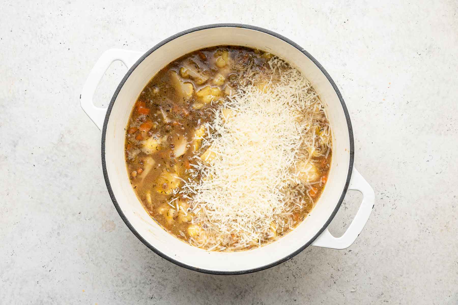 Stirring Parmesan cheese into a pot of lentil cauliflower soup.
