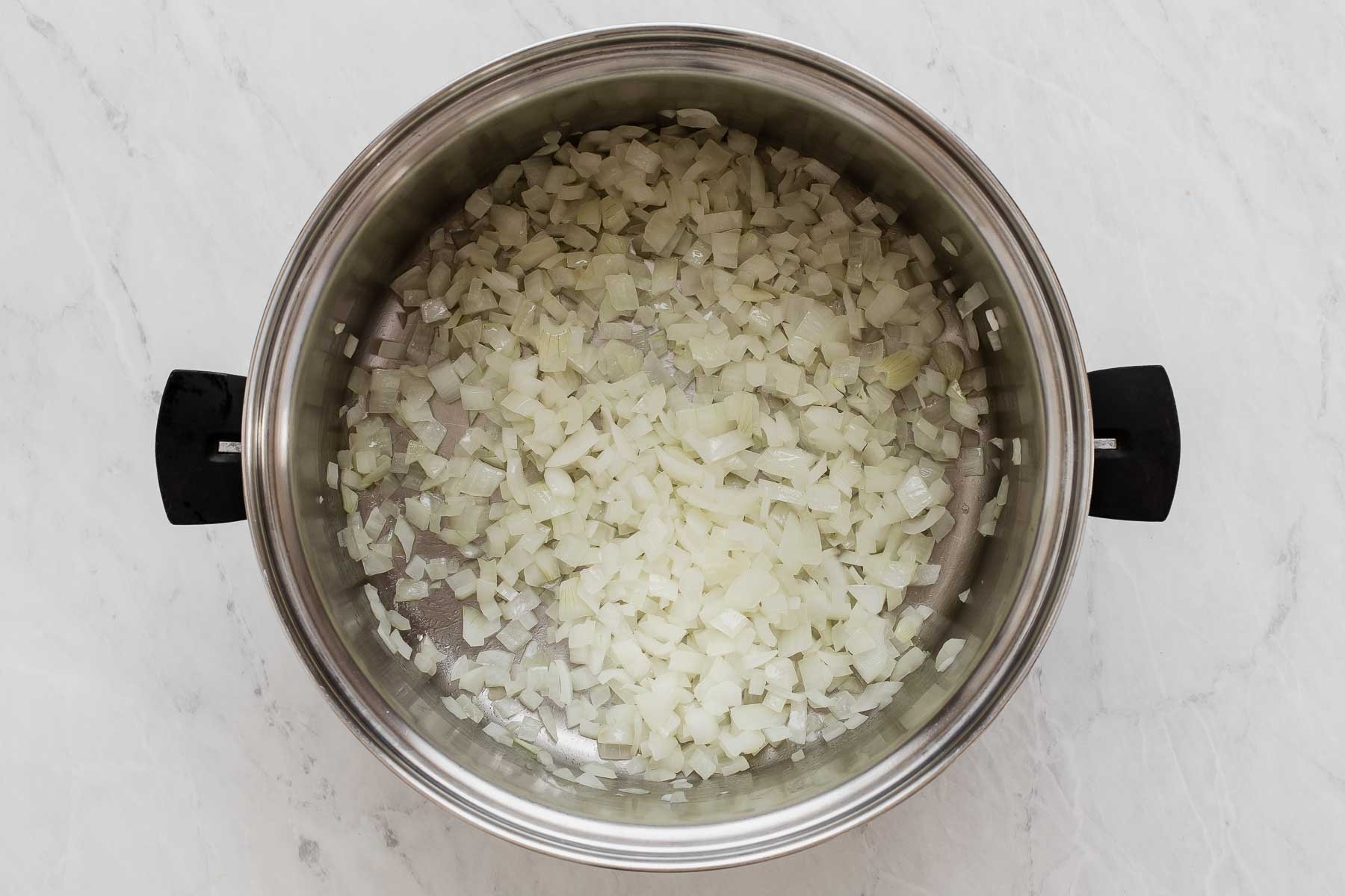 Diced white onions in silver pot cooking.