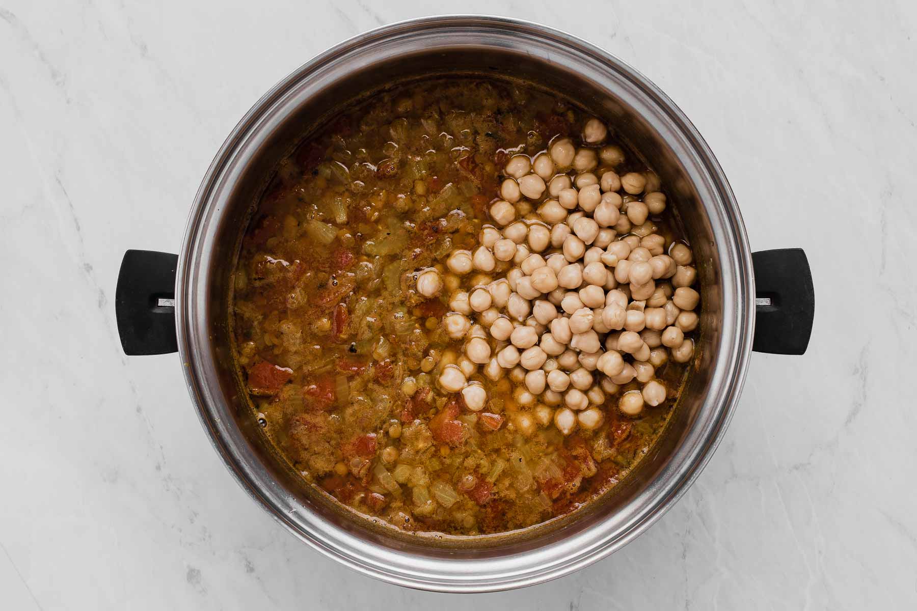 Adding chickpeas to a pot of brown stew on the stove.