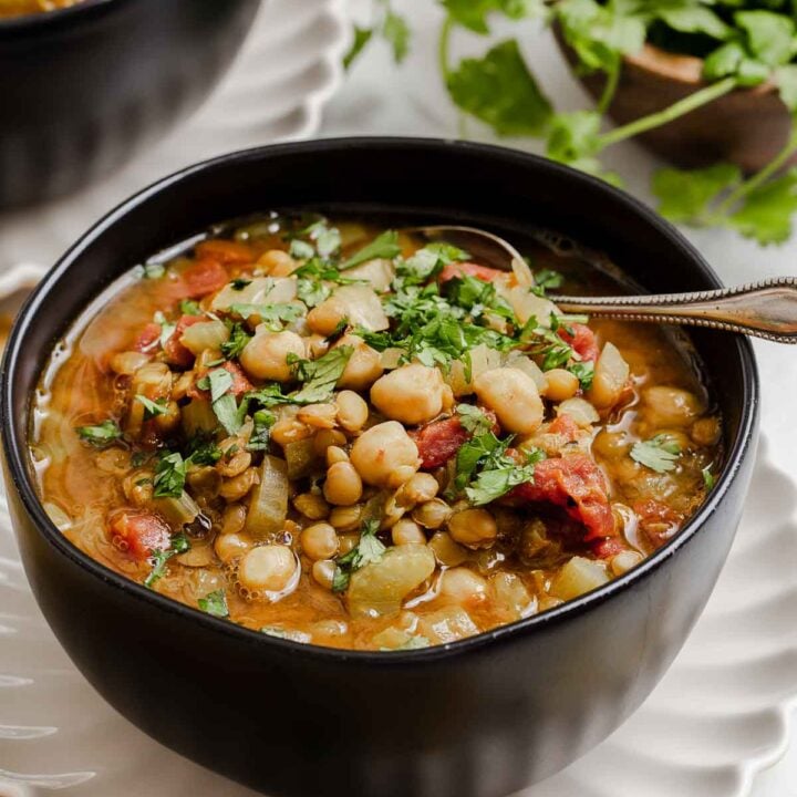 Black bowl with Moroccan chickpea stew with lentils, tomatoes and greens on side.