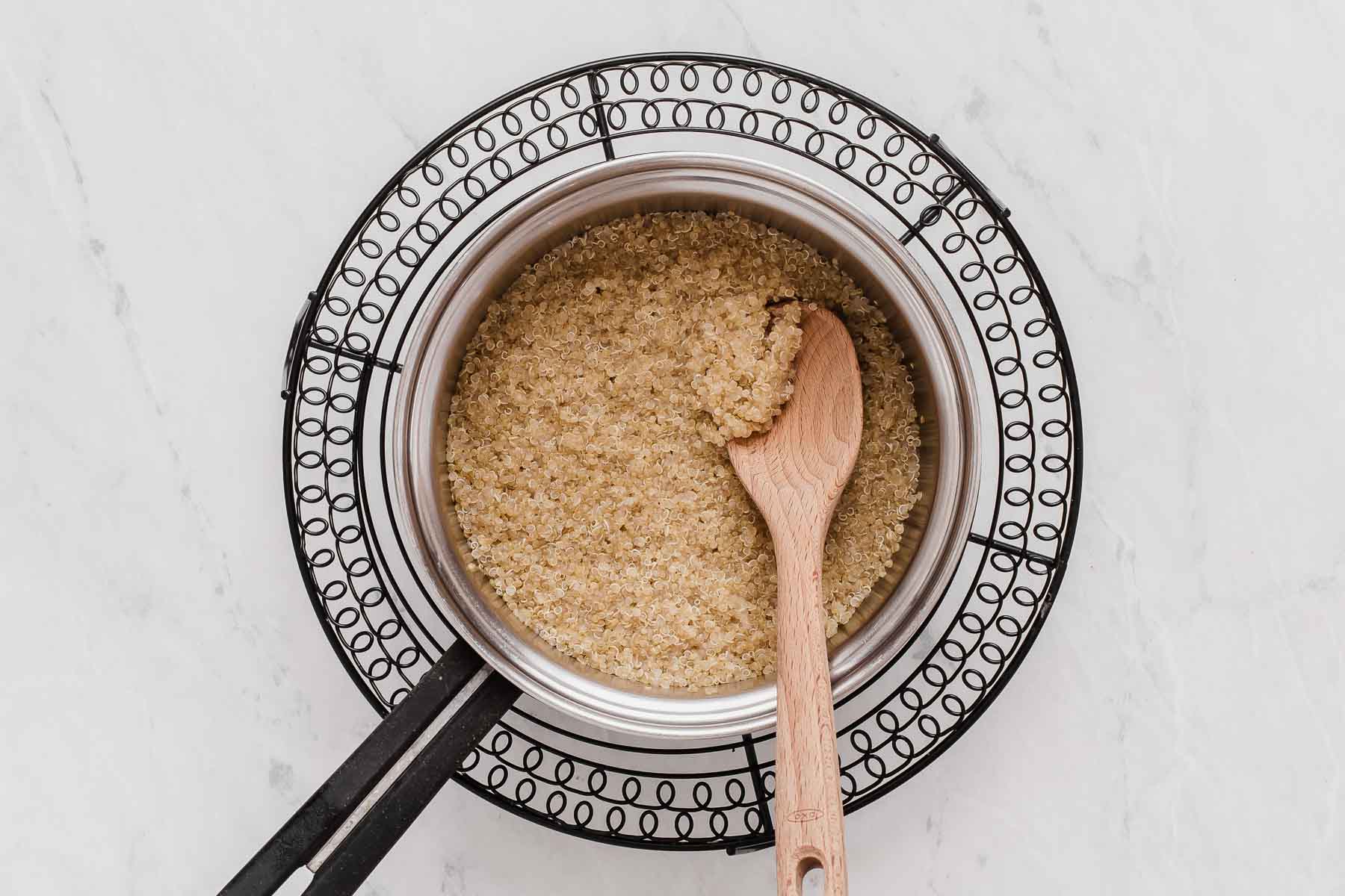 Small pot with freshly cooked quinoa and a wooden spoon.