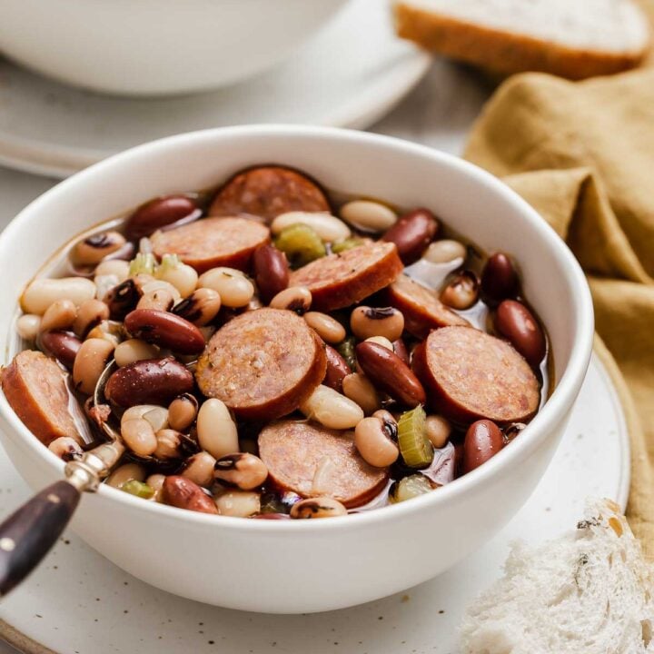 3 Bean Soup with sliced sausage served in a white bowl with crostini on side.
