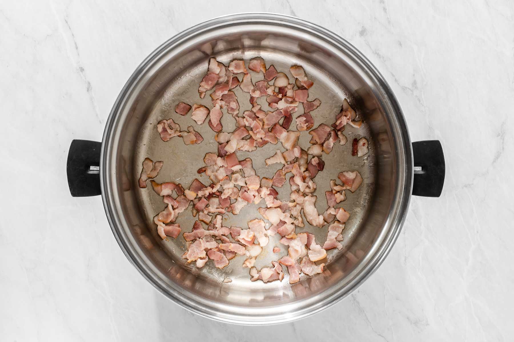 Sliced bacon lardons sautéing in a silver pot with black handles.