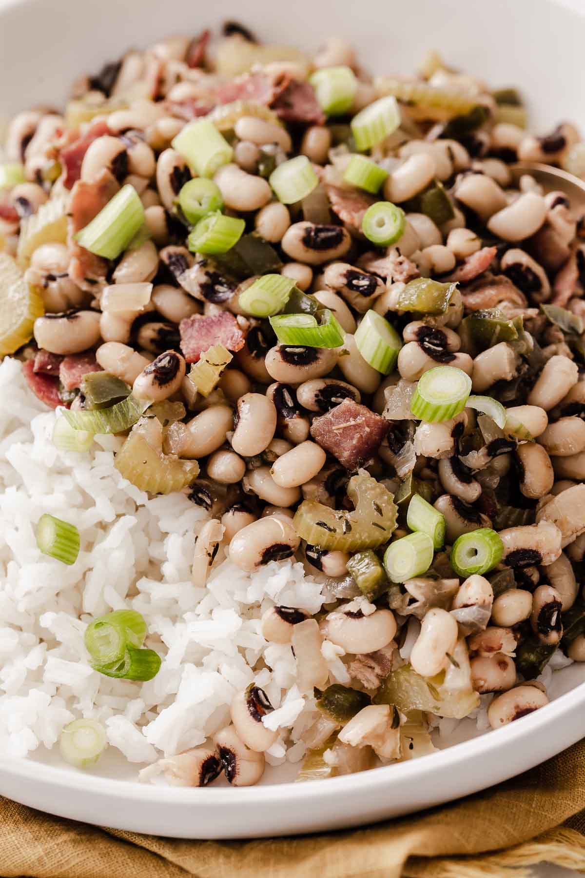 Close up of Hoppin John served over rice with sliced scallions on top.