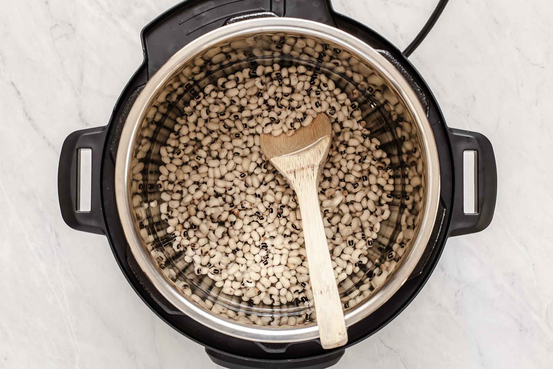 Raw black eyed peas in an instant pot with a wooden spoon.