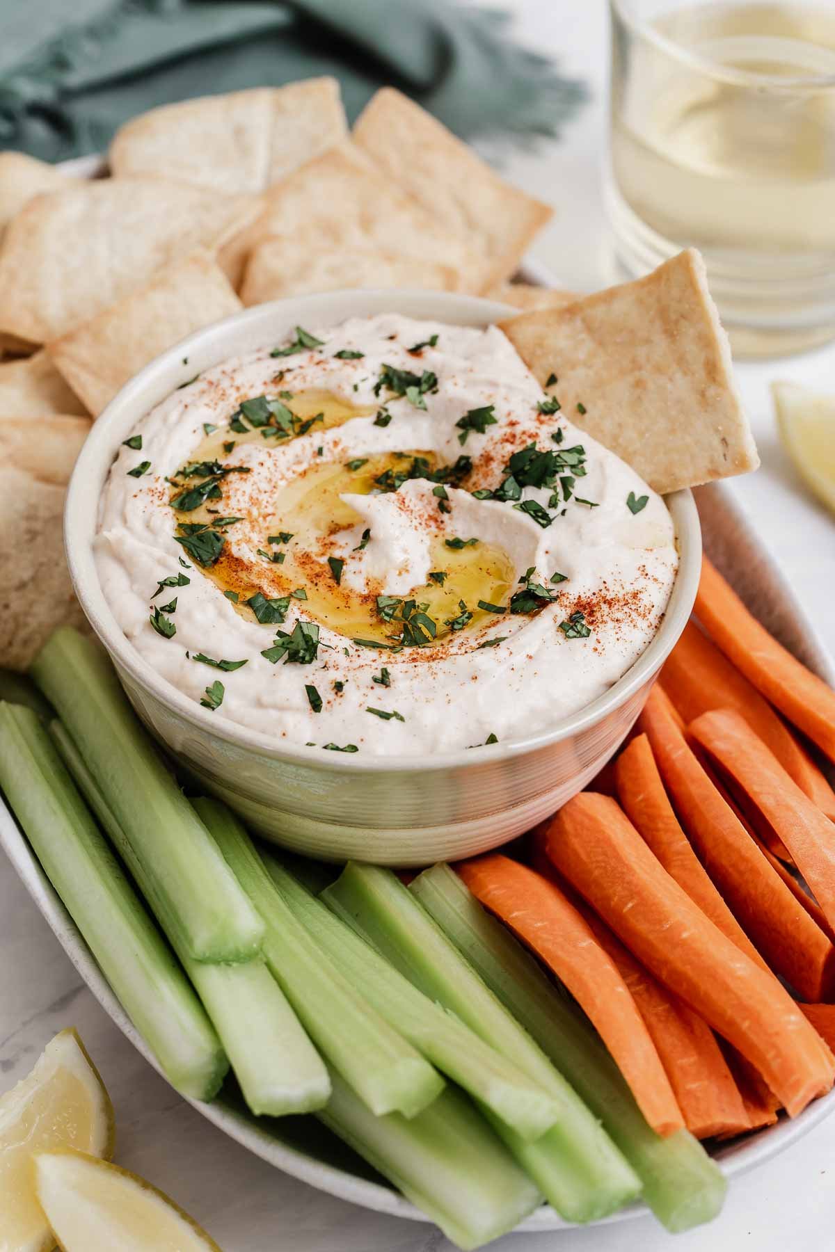 Bowl of white bean hummus with pitas, carrots and celery surrounding.