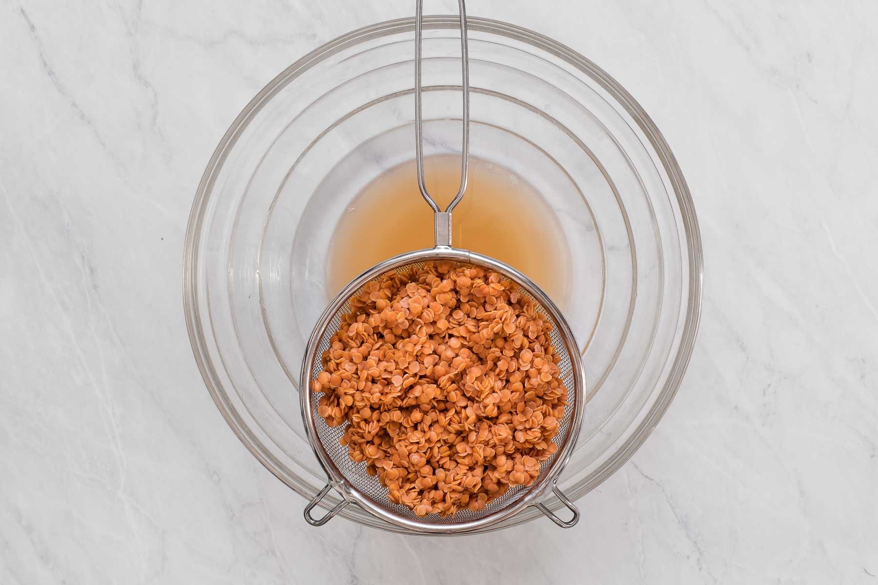Soaking red lentils in a clear bowl with strainer on top.