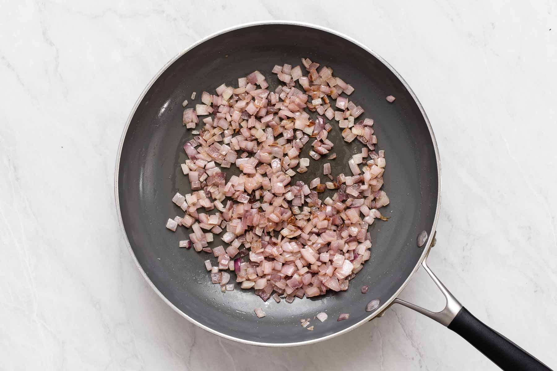 Sautéing red onions in a grey skillet until golden brown.