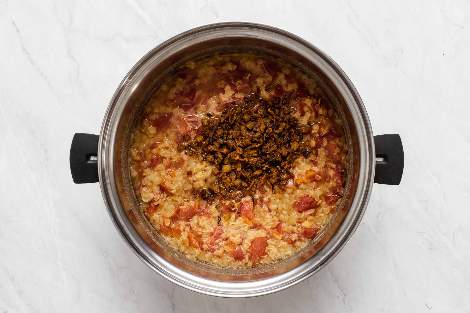 Stirring cooked golden brown onions into pot with cooked red lentils and tomatoes.