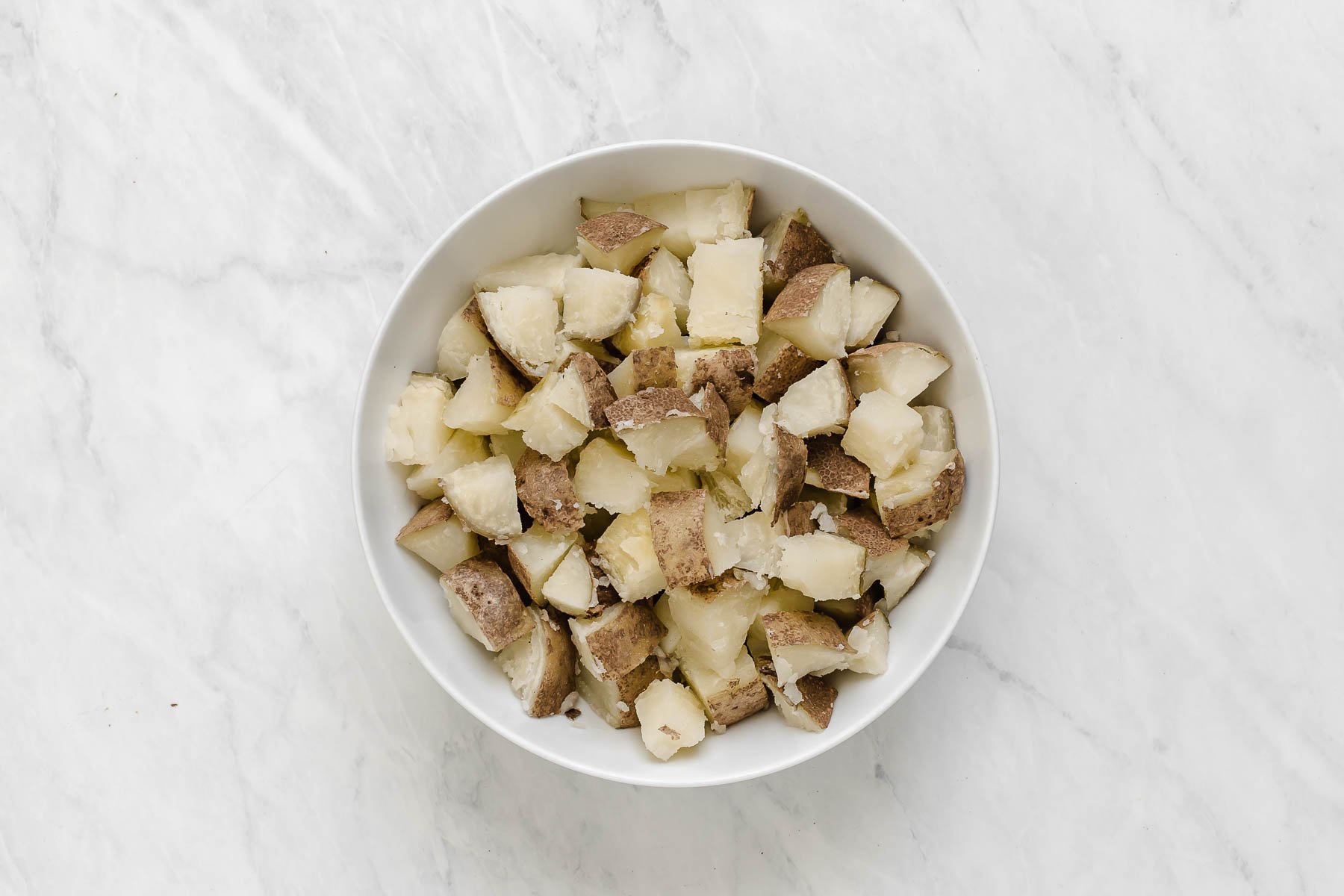 Diced potatoes with the skin on, piled in a small white bowl.