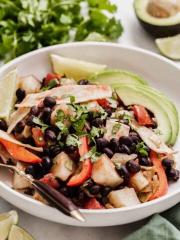 White plate with black beans, potatoes, red peppers and avocado piled up.