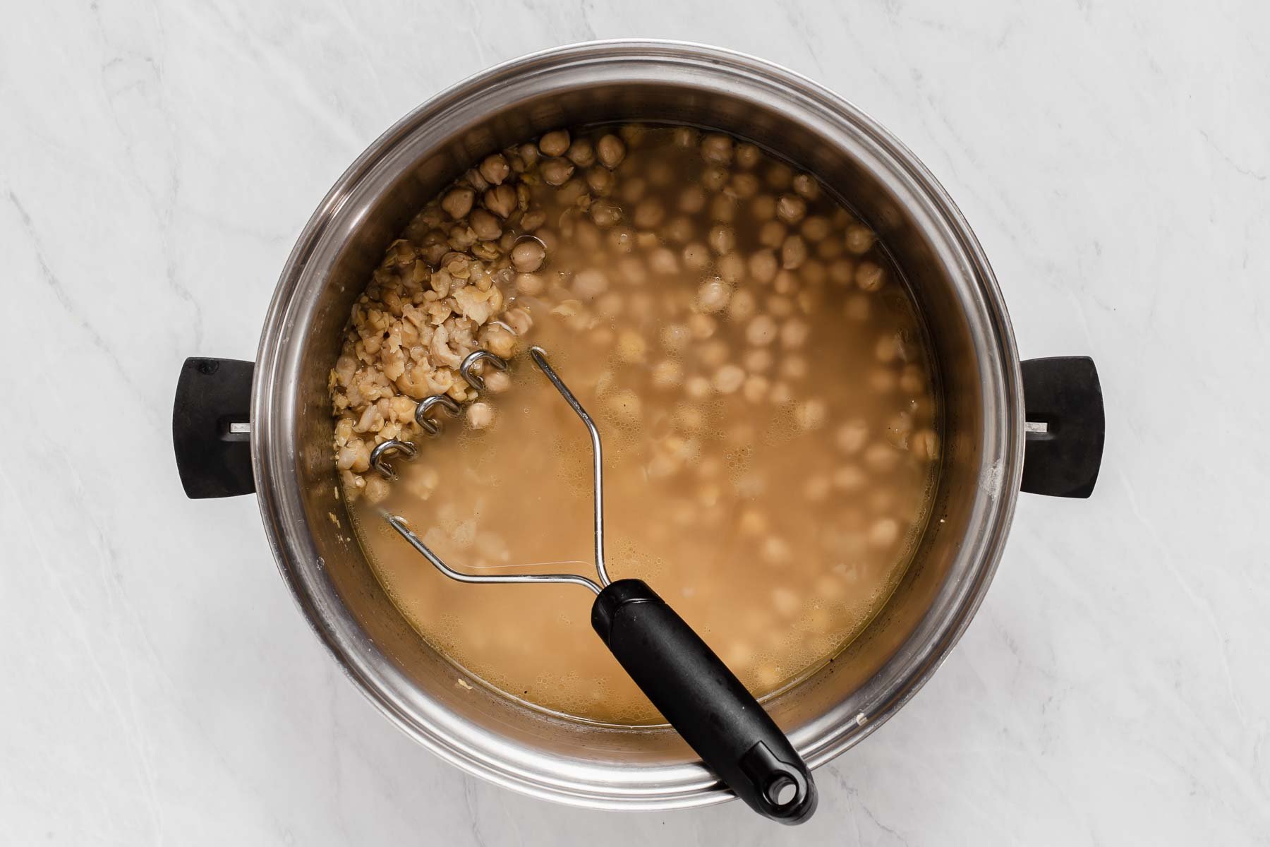 Soup pot with chickpeas and potato masher.