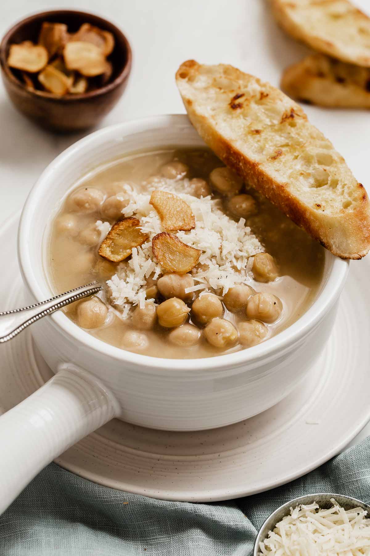 Image of chickpea soup with Parmesan and toasted garlic chips on top of bowl.