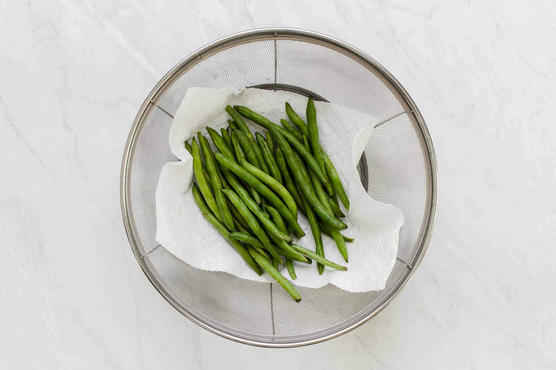 Green beans in a colander on a paper towel.
