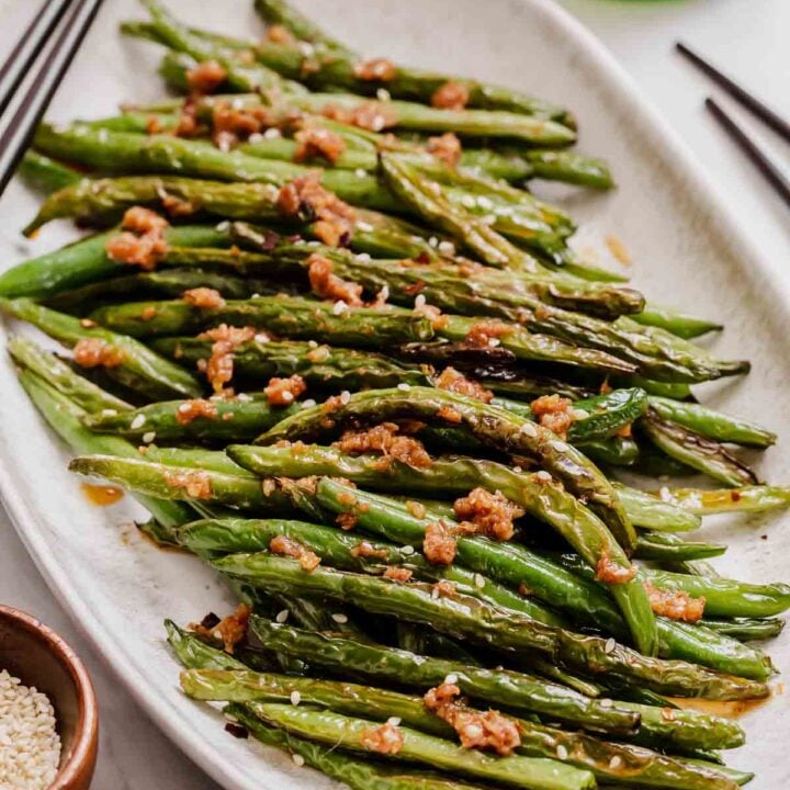 Oval plate of Asian green beans with chopsticks.