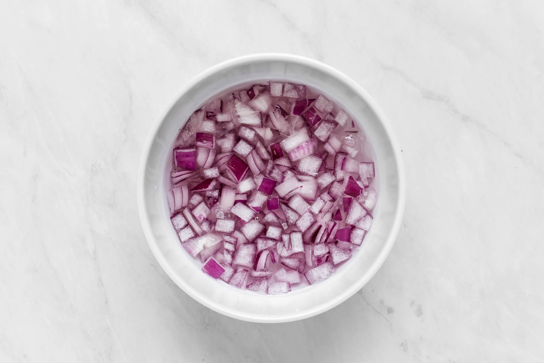 Diced red onions in bowl covered with warm water.