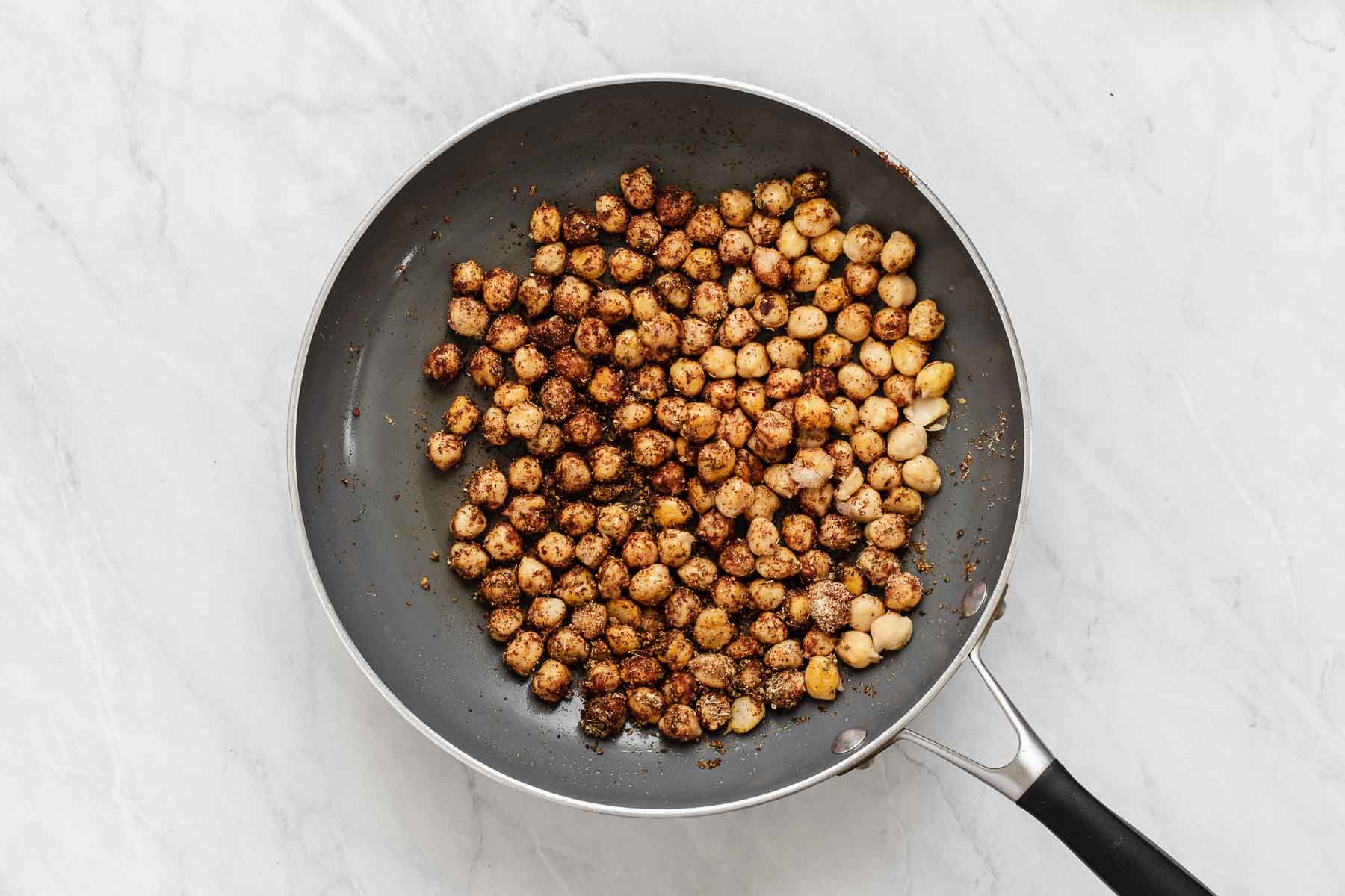Chickpeas in a grey skillet with spices.