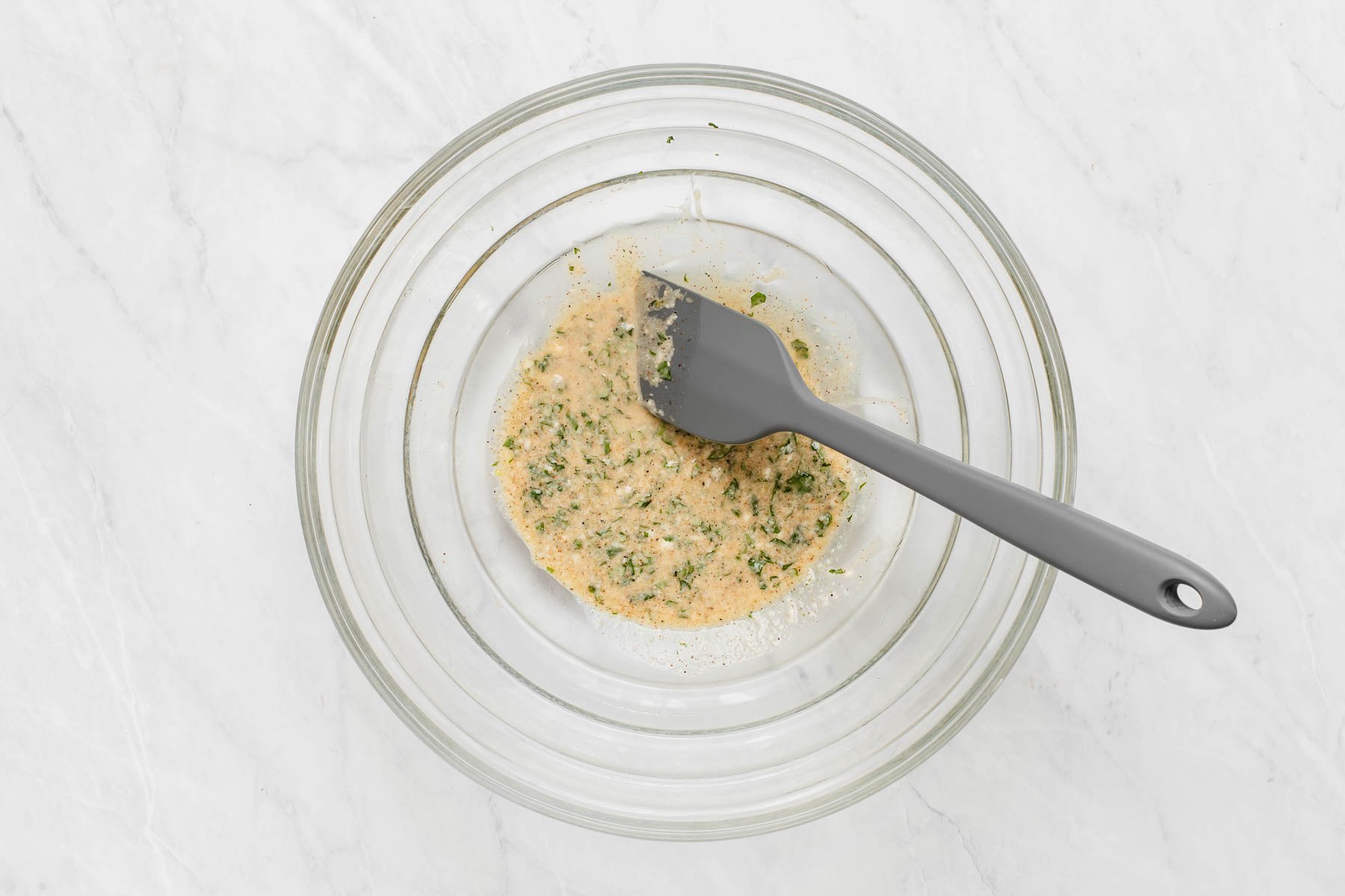 Creamy dressing with cilantro flecks in a clear glass bowl with spatula.