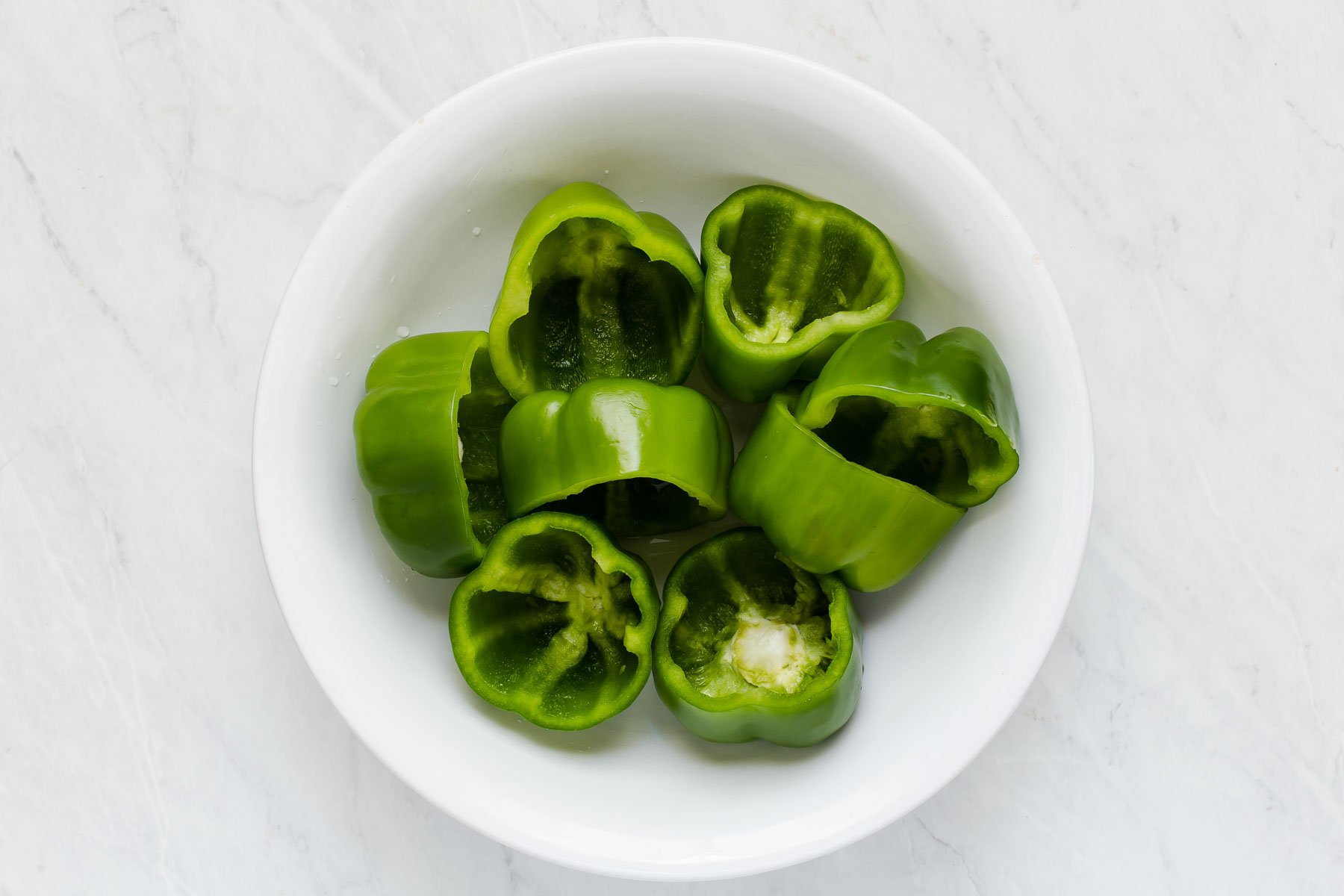 Eight green bell peppers, cut in half, cleaned and placed in a white bowl.