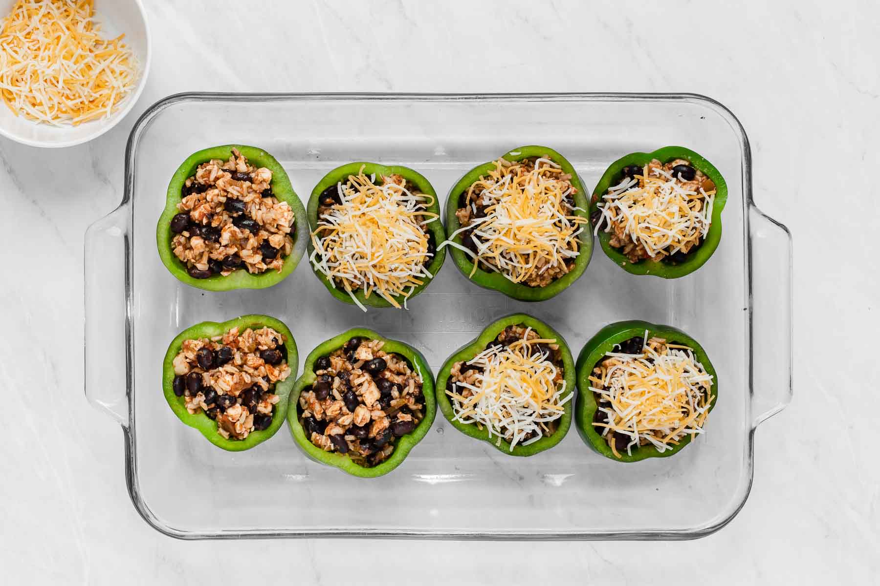 Pan of stuffed peppers with chicken being topped with cheese.