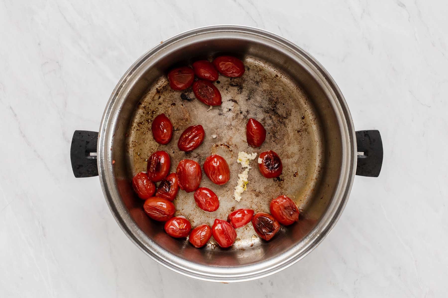 Pot with grape tomatoes and minced garlic, sautéing.