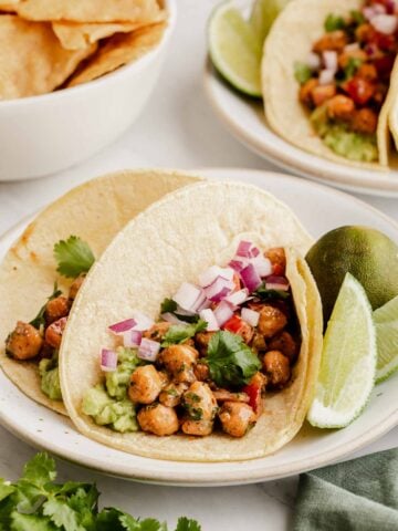 Two chickpea tacos on a plate with sliced lime on side.