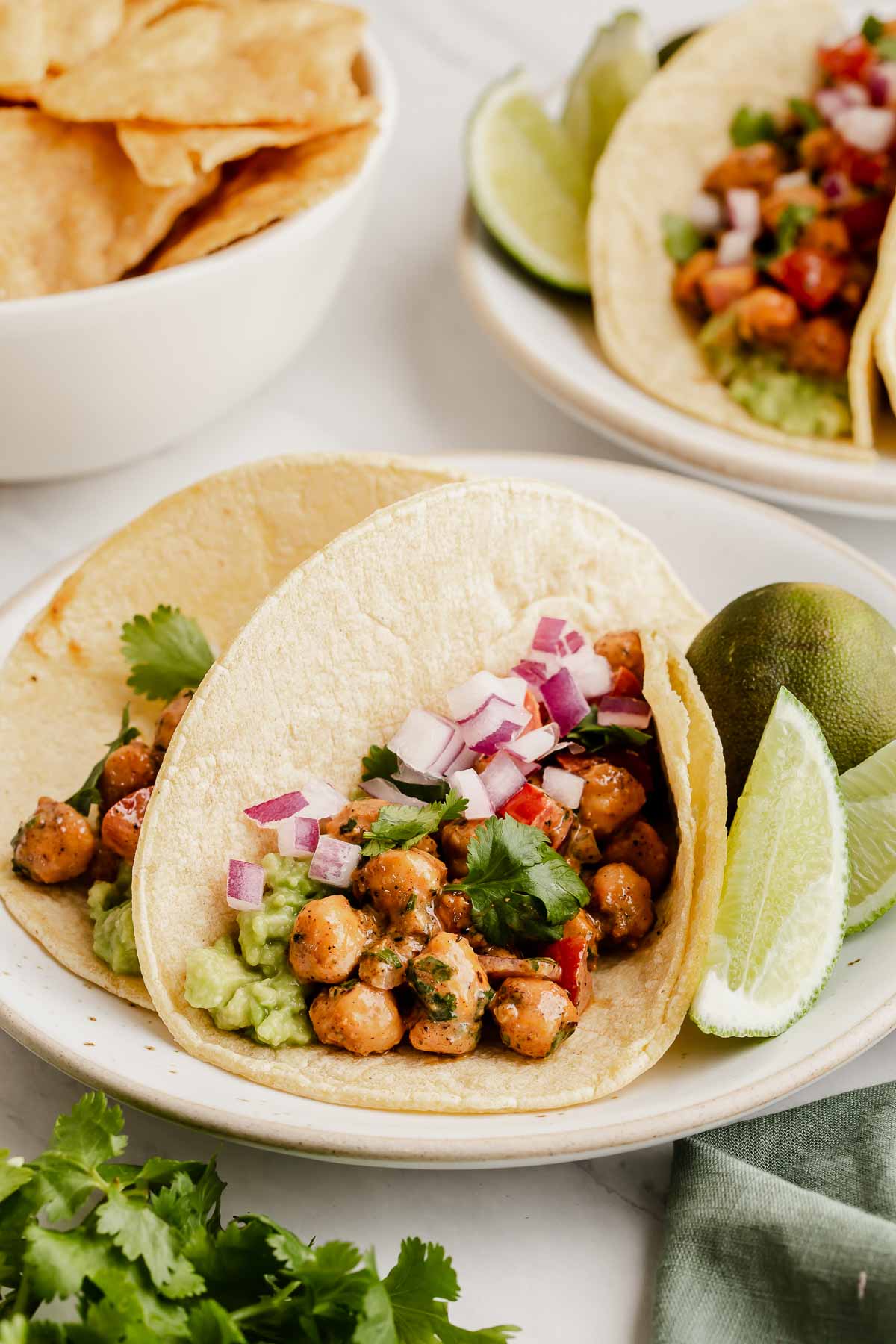 Two chickpea tacos on a plate with sliced lime on side.
