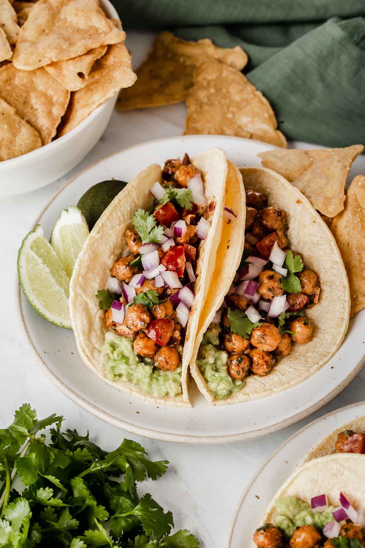 Two chickpea tacos side by side on plate with sliced lime on side.