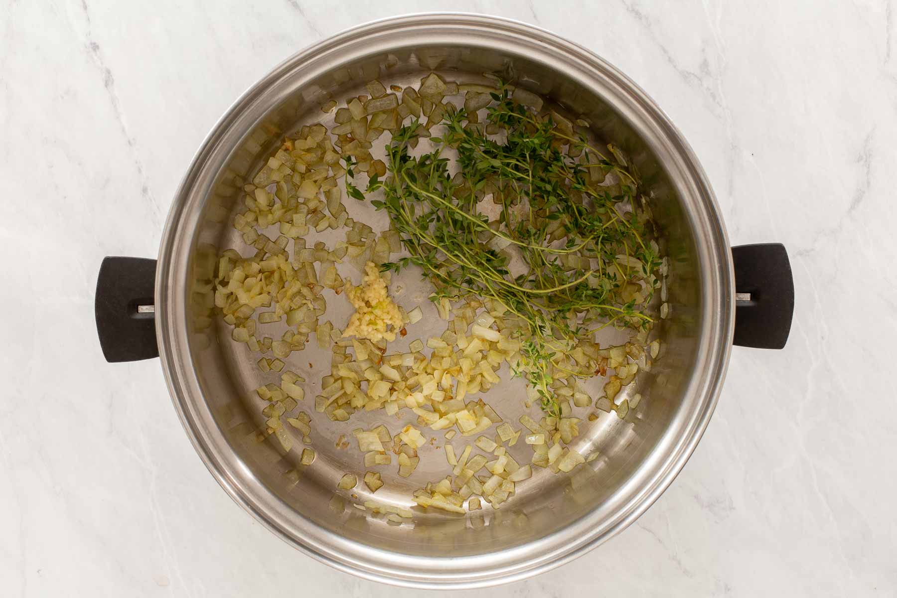 Silver pot with onions, garlic and thyme sprigs.