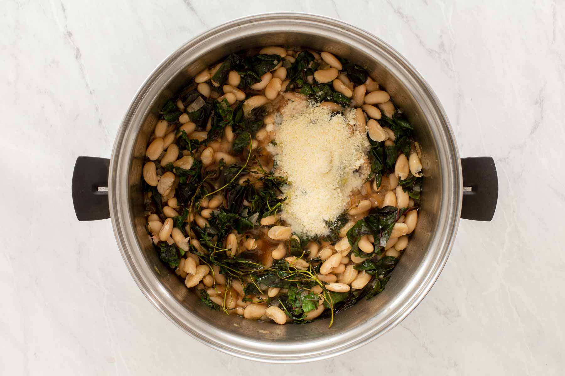 Adding Pecorino to soup pot with white beans and leafy greens.