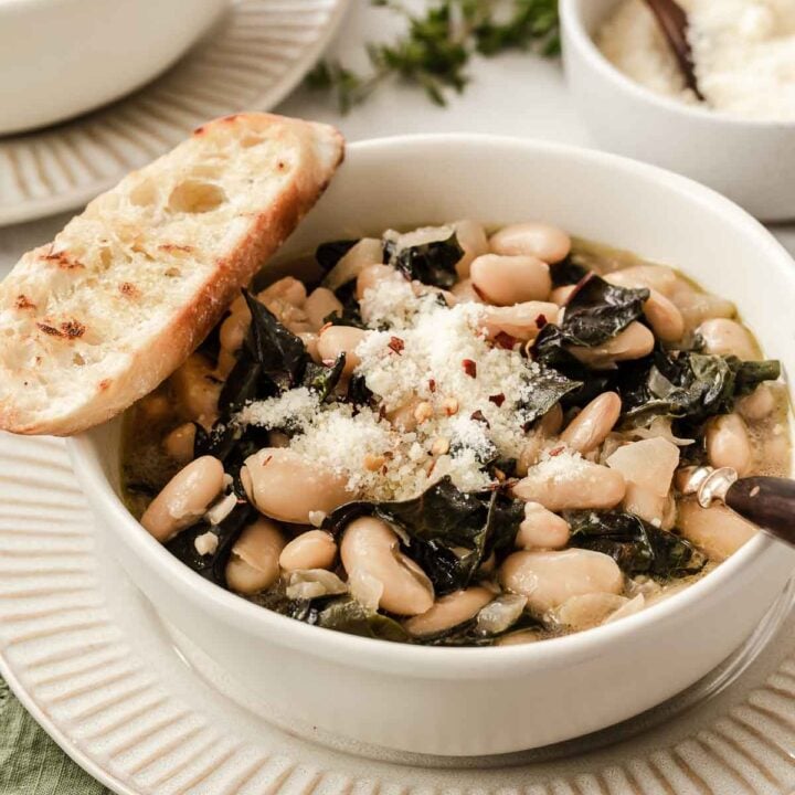 Bowl of white beans and greens with Parmesan cheese and bread slice on top.