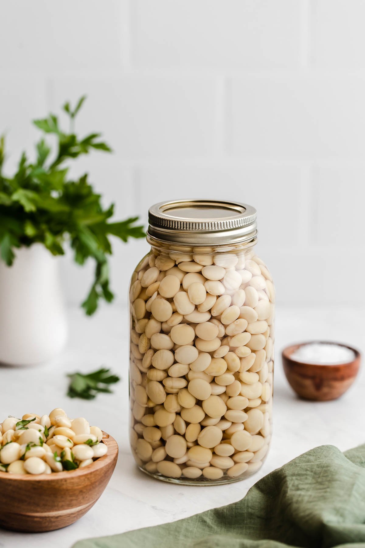 Glass mason jar full of lupini beans with herbs in background.