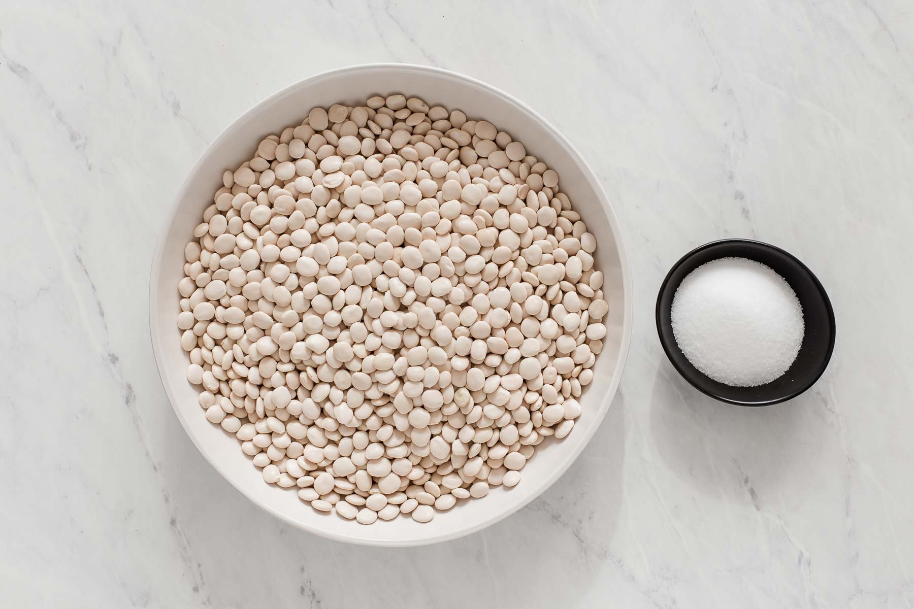 Bowl of dry white beans and small bowl of salt.