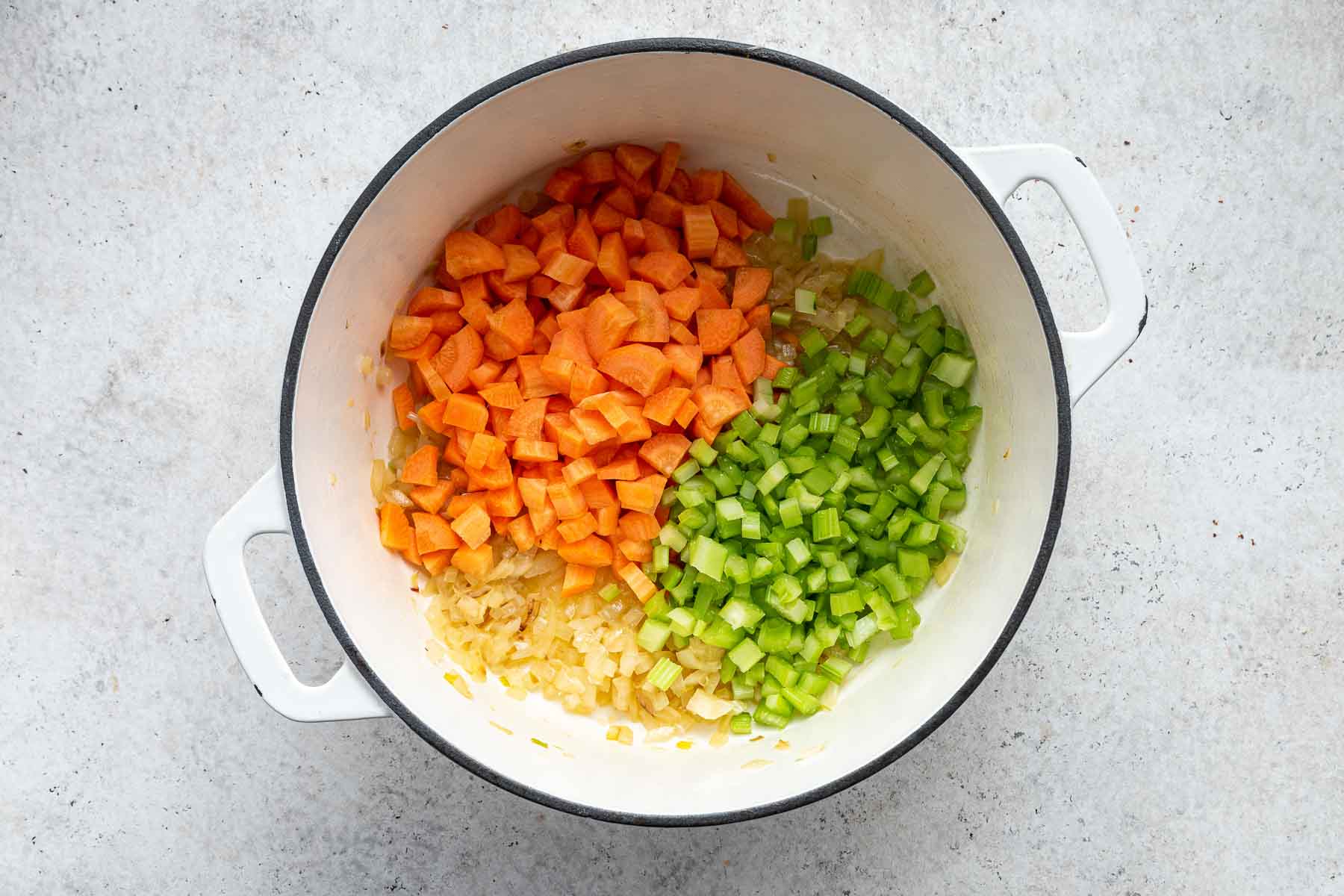 Diced carrots and celery on top of caramelized onions in white pot.