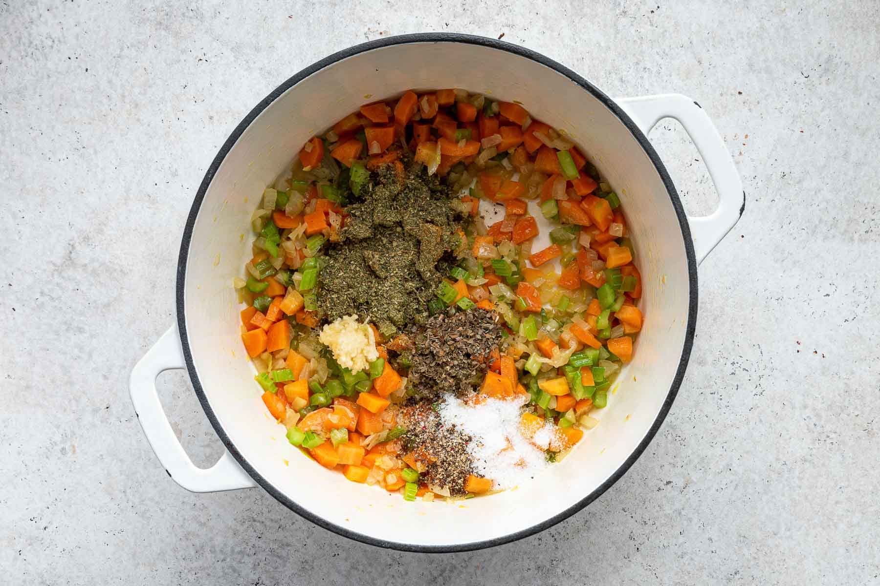 Dried herbs and spices on top of cooked vegetables in soup pot.