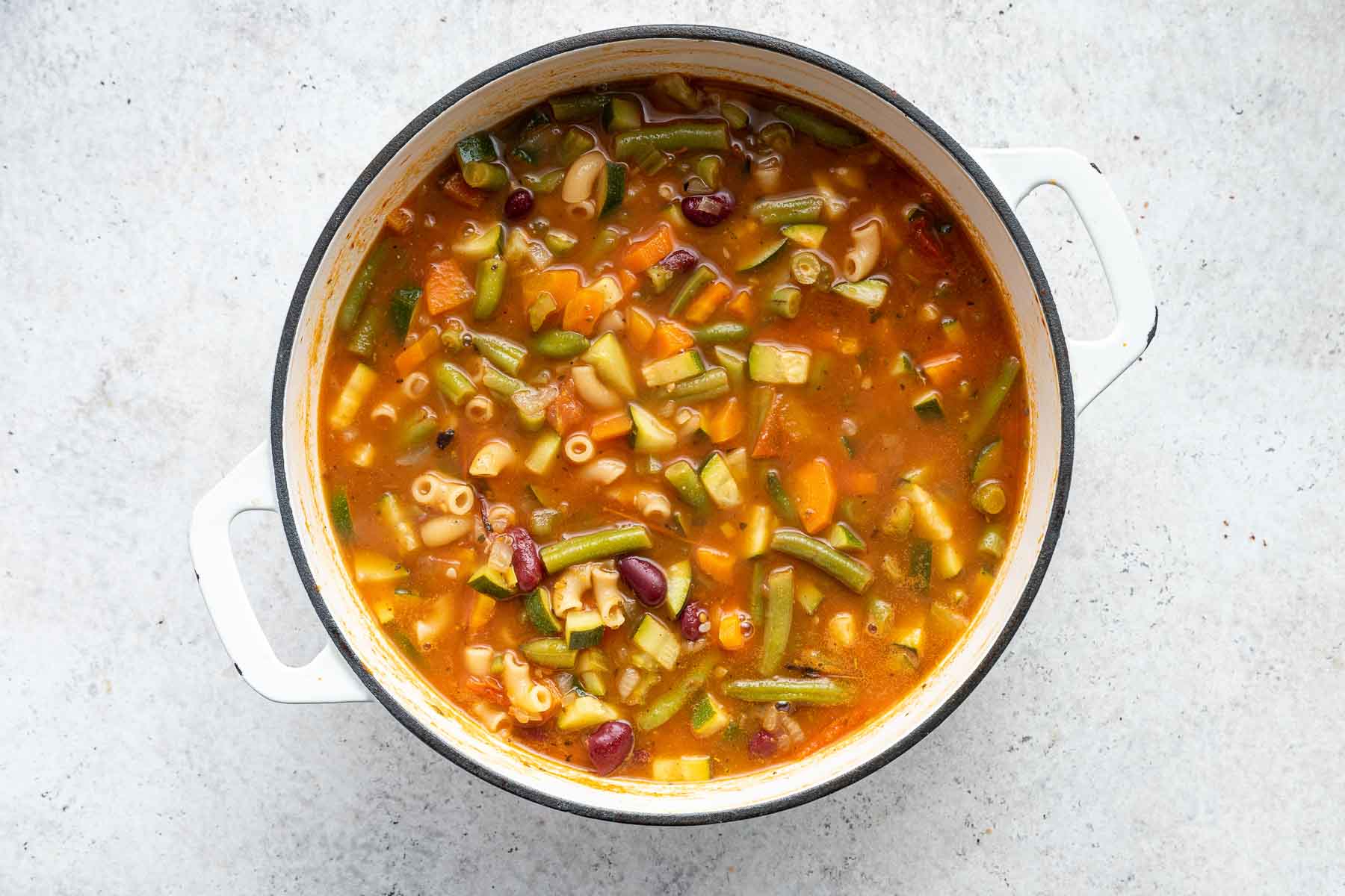Horizontal image of minestrone soup in white pot.