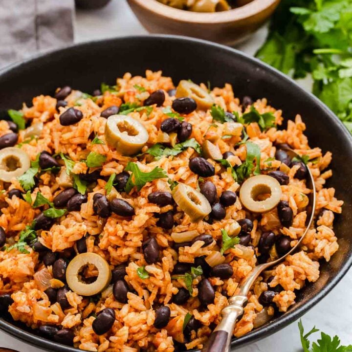 Black bowl with Spanish rice and beans with sliced olives on top.