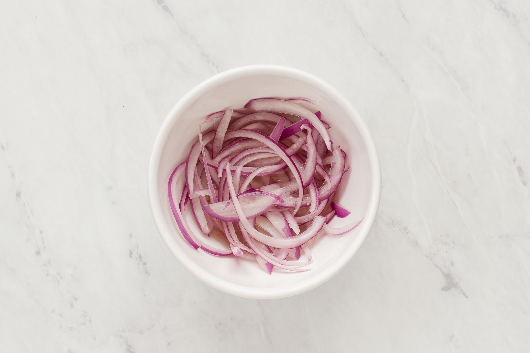 Thinly sliced red onion in small white bowl.
