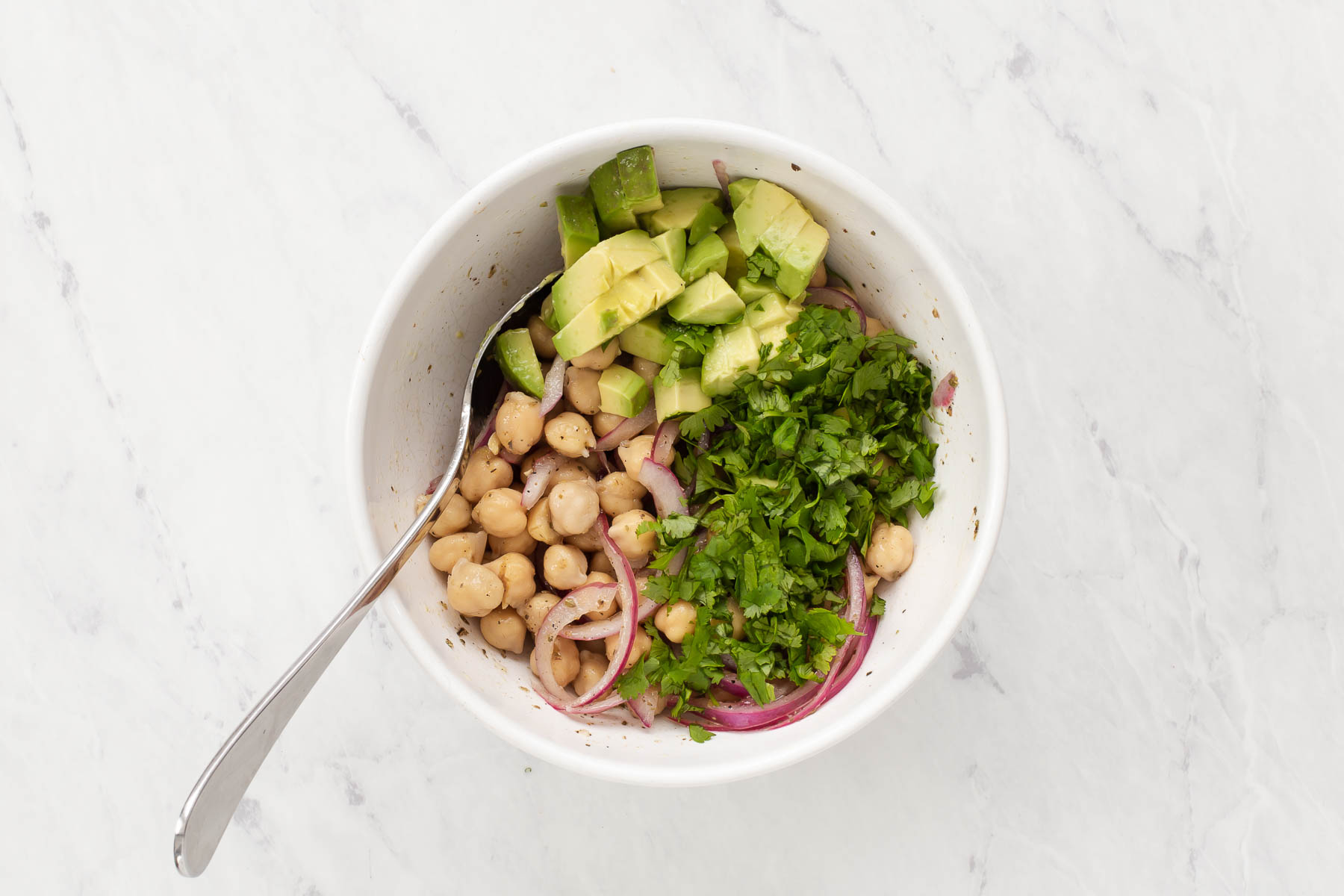 Avocado chickpea salad in white bowl topped with cilantro and a spoon.