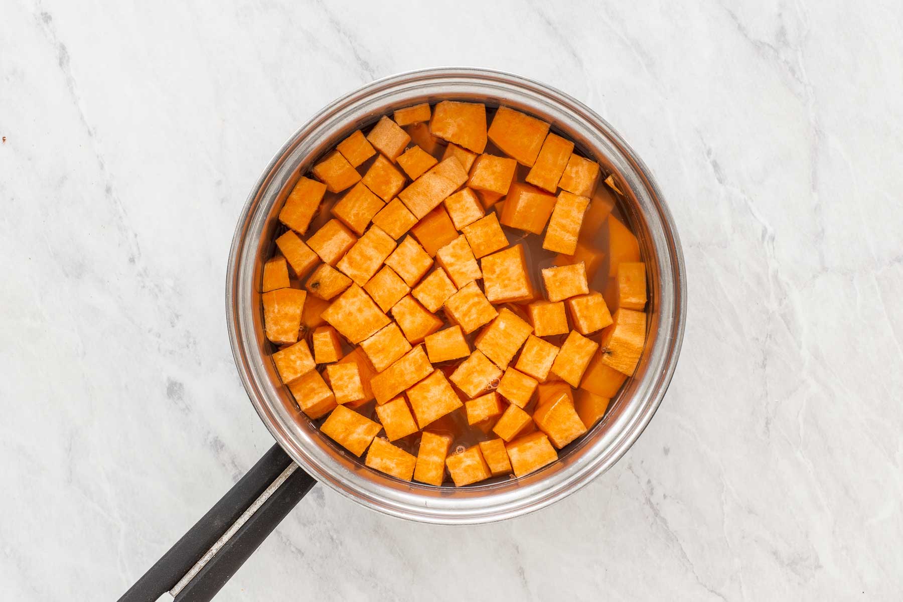 Diced sweet potatoes in small silver pan covered with water.