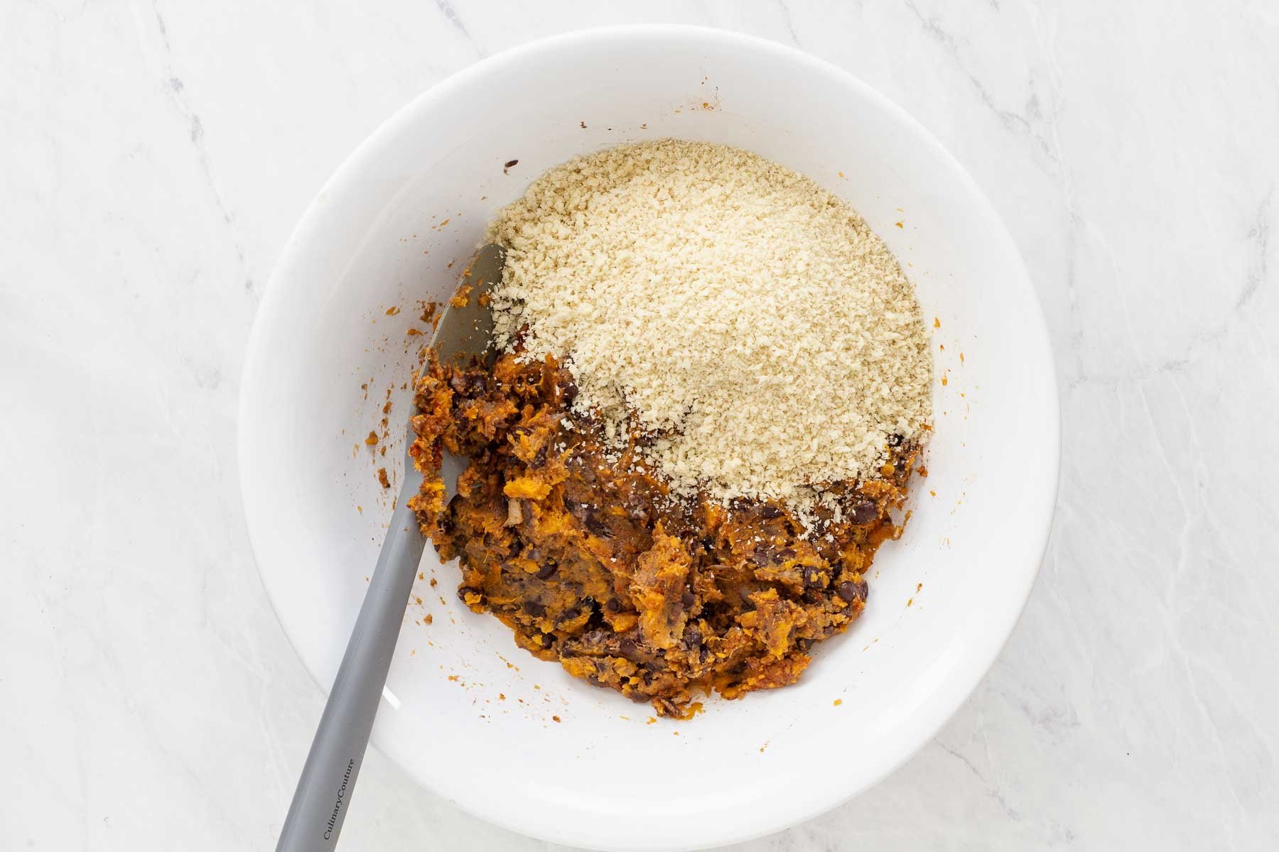 Stirring panko bread crumbs into bowl with mashed sweet potatoes and black beans.