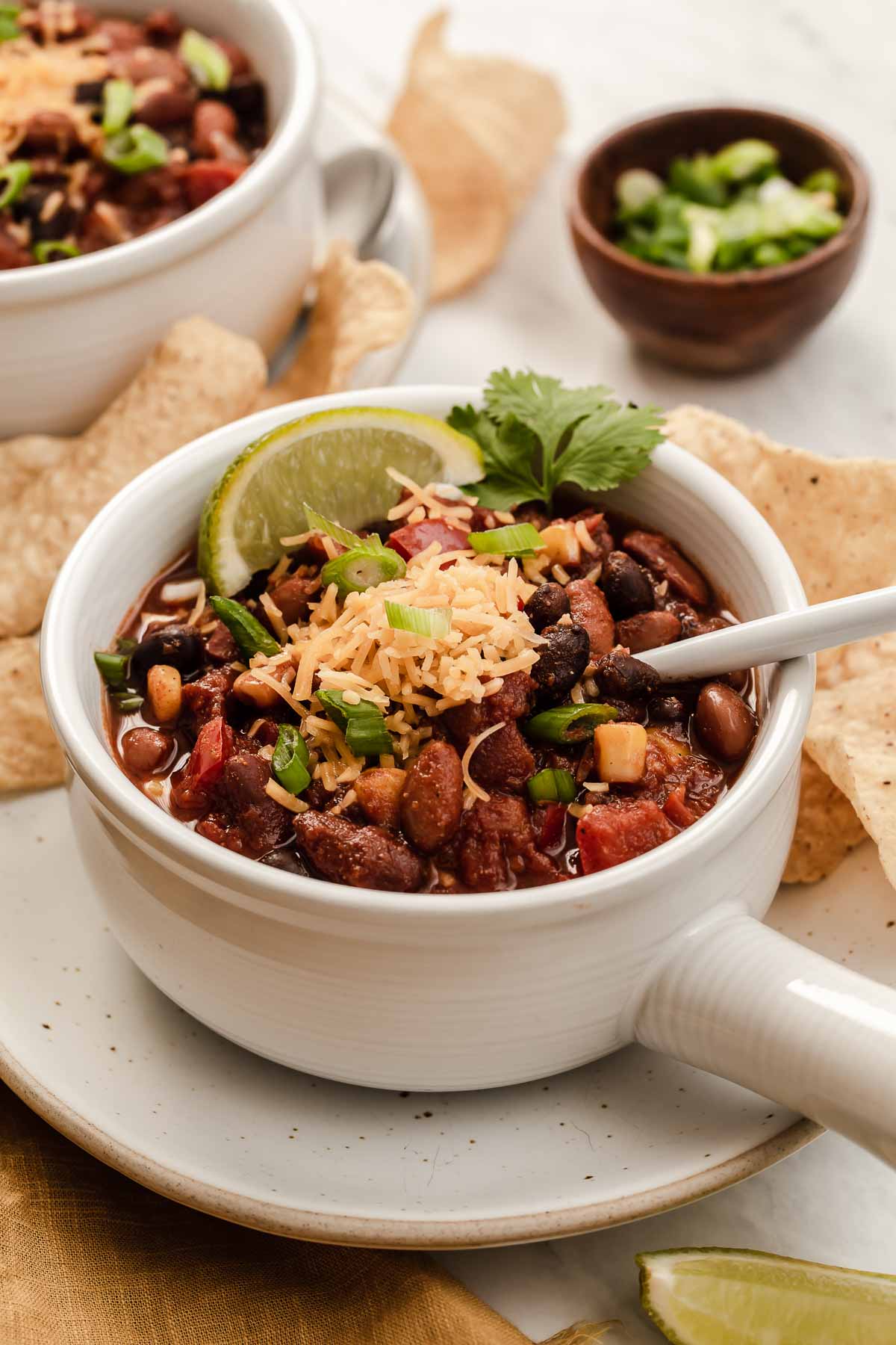 White bowl of chunky vegetarian chili slow cooker topped with cheese and lime.