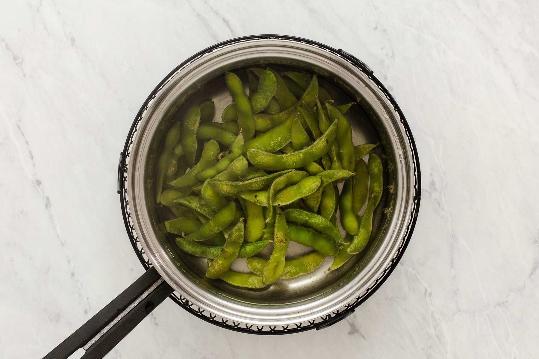 Green soybean pods in a pot of boiling water.