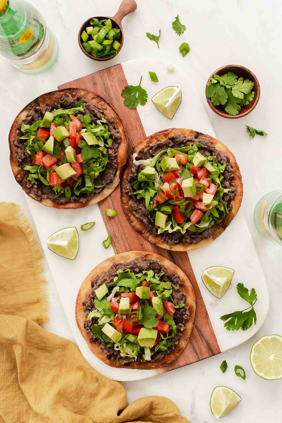 Overhead vertical image of black bean tostadas with cilantro sprinkled everywhere.