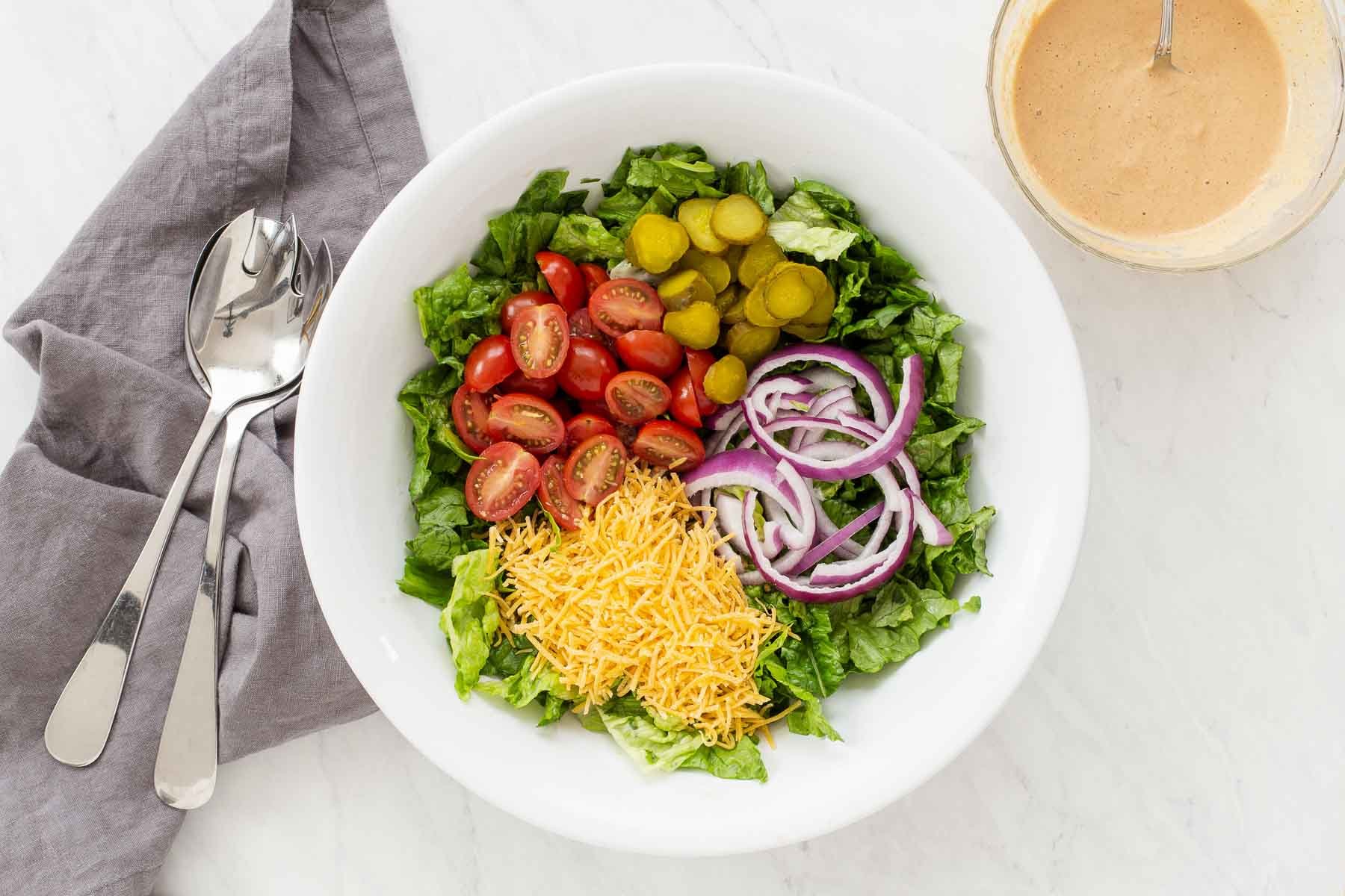 Salad bowl with shredded cheese, tomatoes, pickles and onions.